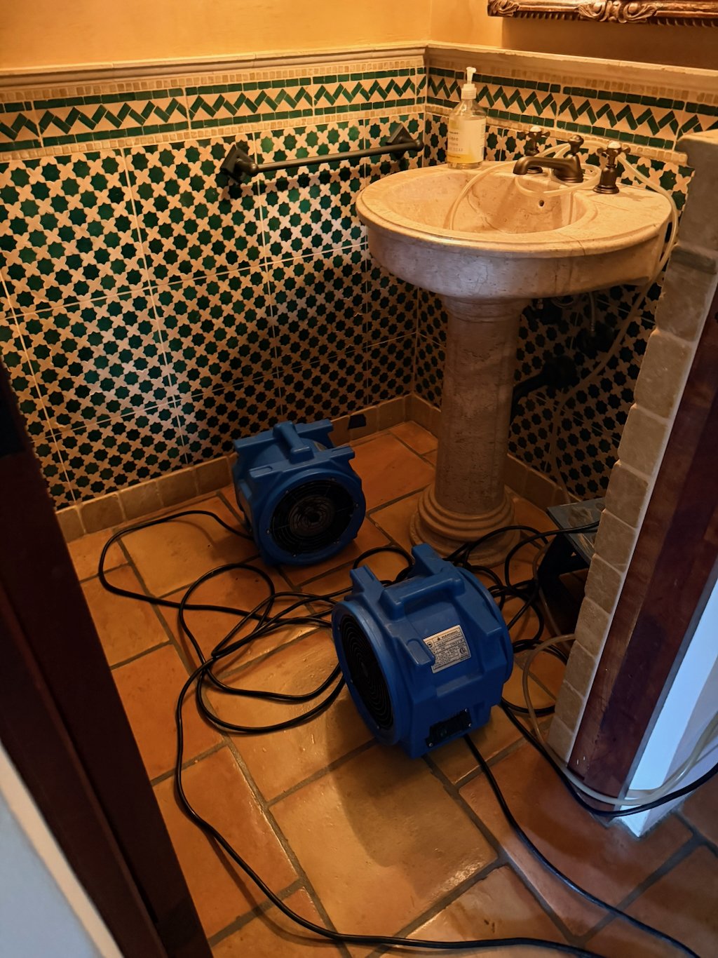 Air movers drying a Saltillo tile floor beneath a travertine pedestal sink and hand-set tile in a luxury Paradise Valley powder room